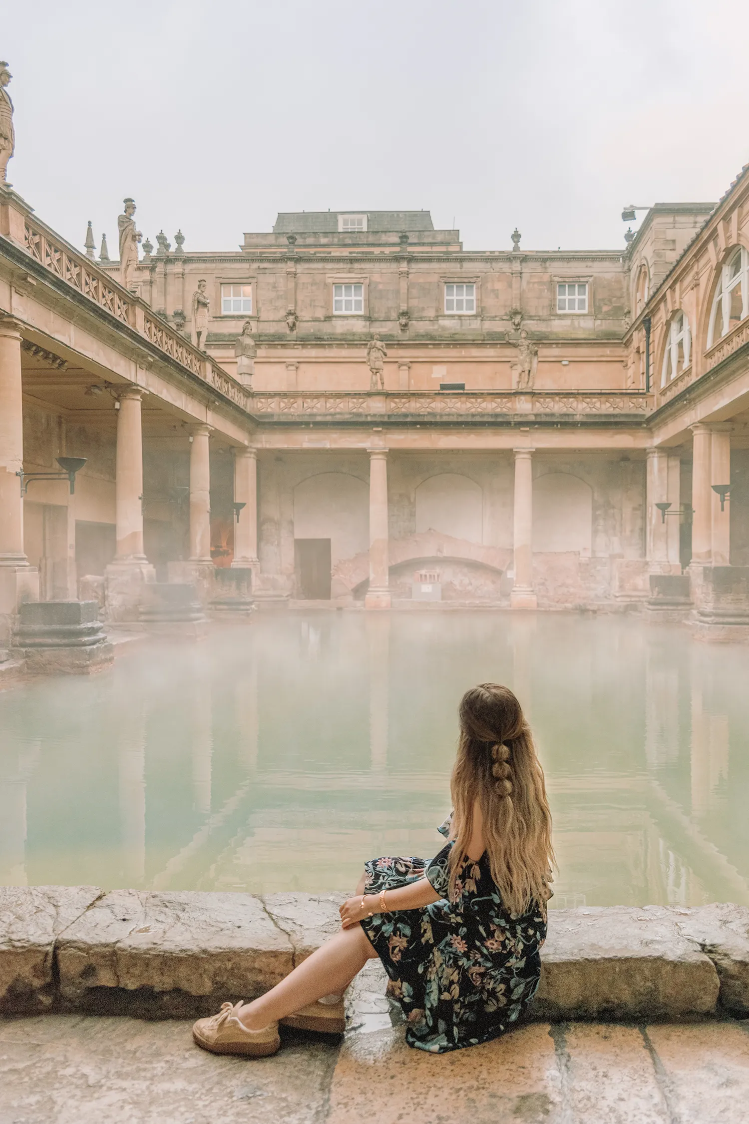 Ida Josefin Eriksson sitting beside the historic Roman Baths in Bath, England, overlooking the steaming Great Bath.