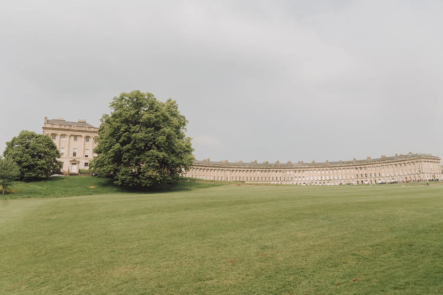 The Royal Crescent in Bath, England, a sweeping row of Georgian townhouses overlooking a large green lawn.